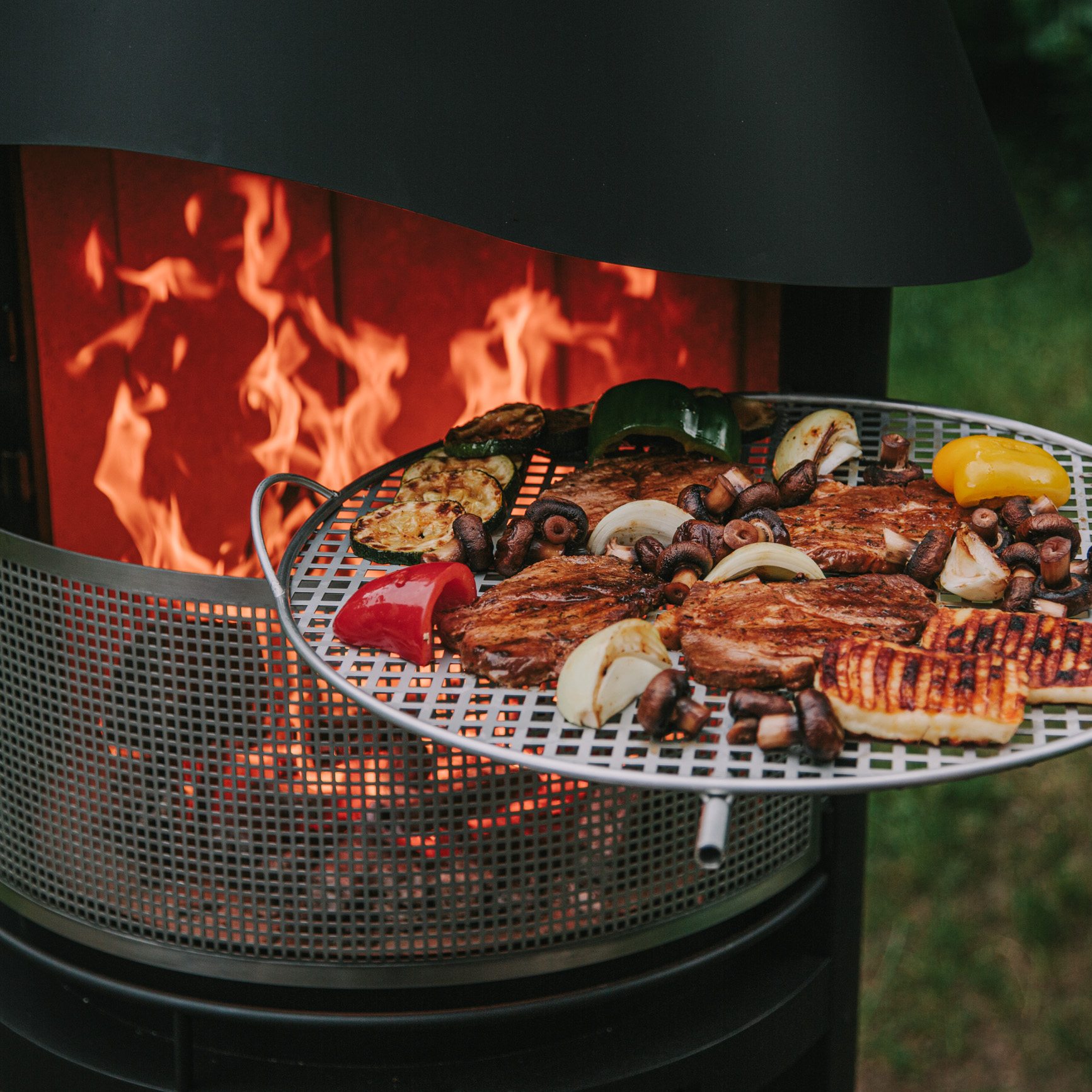 Ein Ausschnitt des Grillkamins Zenit mit Feuer und Grillgut im Vordergrund